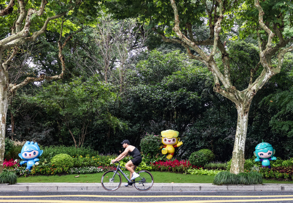 市民在杭州市南山路上一处亚运会主题吉祥物雕塑前骑自行车。